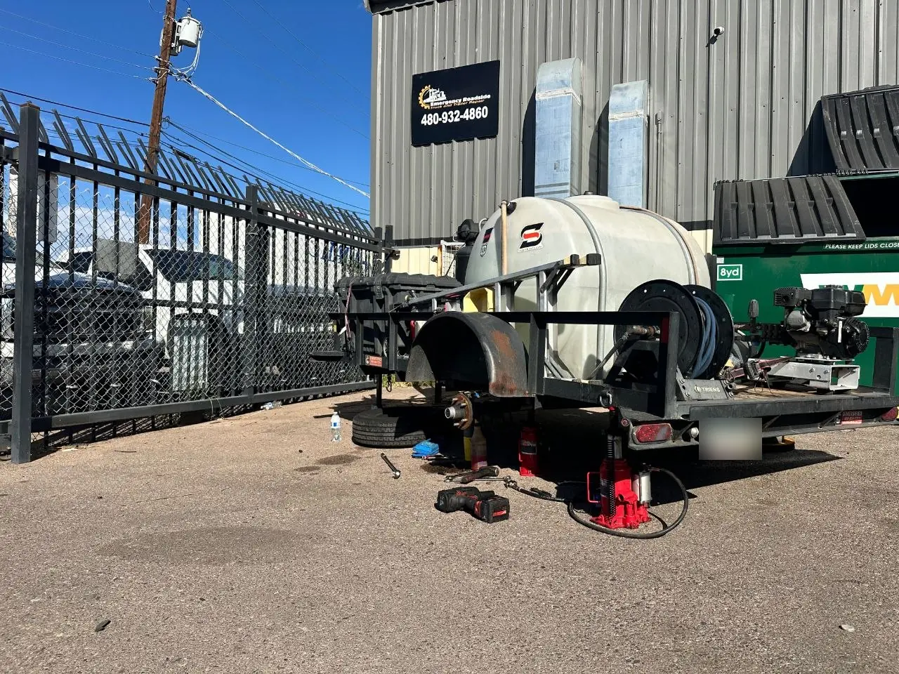 Trailer jacked up with the wheel removed for hub and tire repair in front of the Phoenix shop